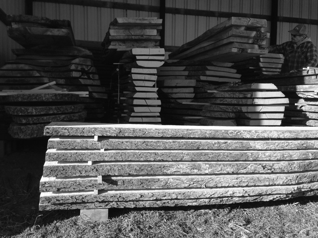 Black and Grey stacked lumber storage in a pole barn with a man in paid shirt and hat in the background 