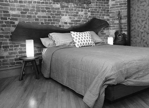 A soft look at our walnut platform bed Bedroom set at side angle with two lights in loft setting with hardwood floor brick background and birch leaf inlayed resin panel