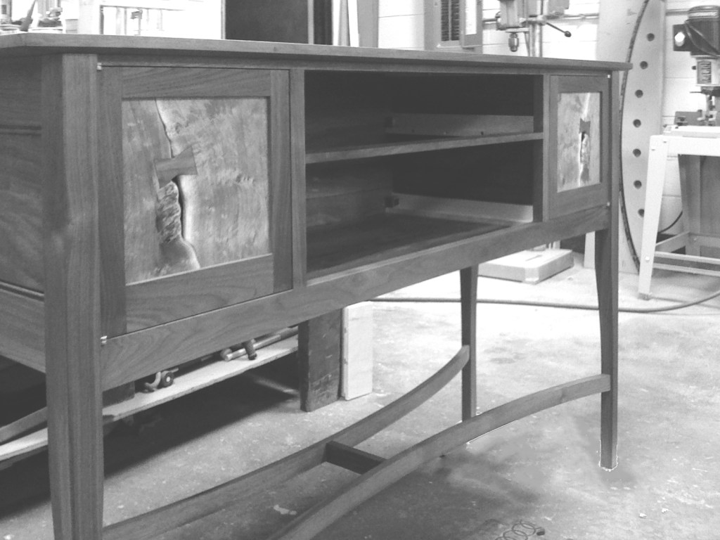 Black and grey mesquite and walnut side board construction with live edge door fronts and bow tie dutchman and woodshop in the background