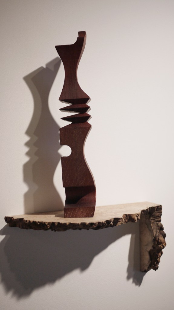 Walnut multi tool sculpture atop maple burl shelf 