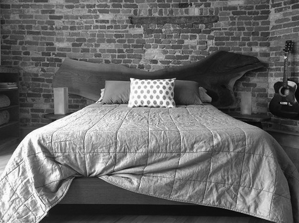 Black and grey platform bed set Live edge walnut headboard platform bed with two side tables and a brick wall in the background and hanging guitar
